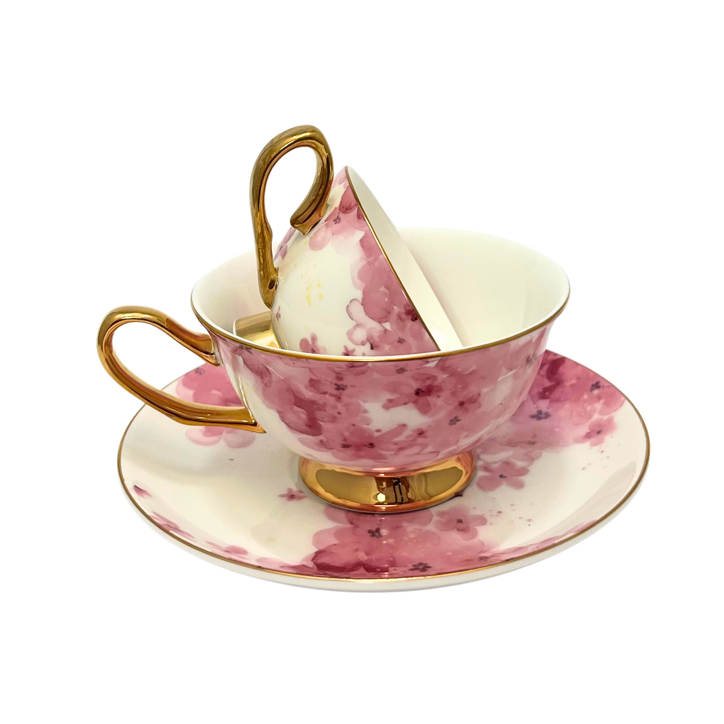 Two teacups with pink flowers on a white background with gold handle and edges. Mini teacup stacked inside standard sized teacup. Sitting on matching pink flower saucer. Isolated on a white background.