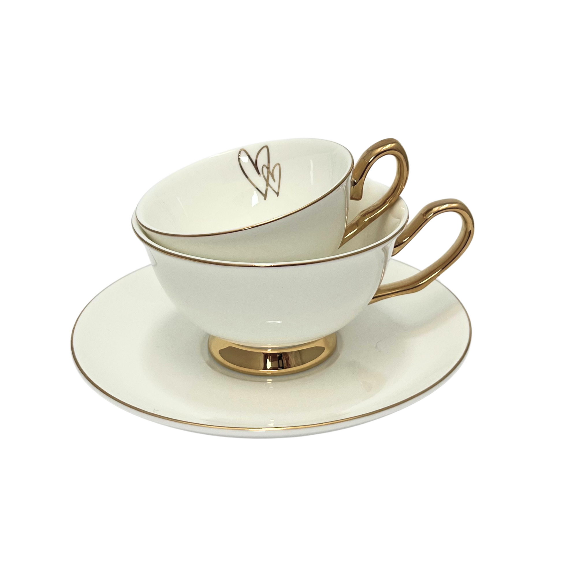 Two white teacups with gold interconnecting love hearts on inside rim.  Gold handle and edges.  Mini teacup stacked inside standard sized teacup.  Sitting on matching white and gold saucer.  Isolated on a white background. 